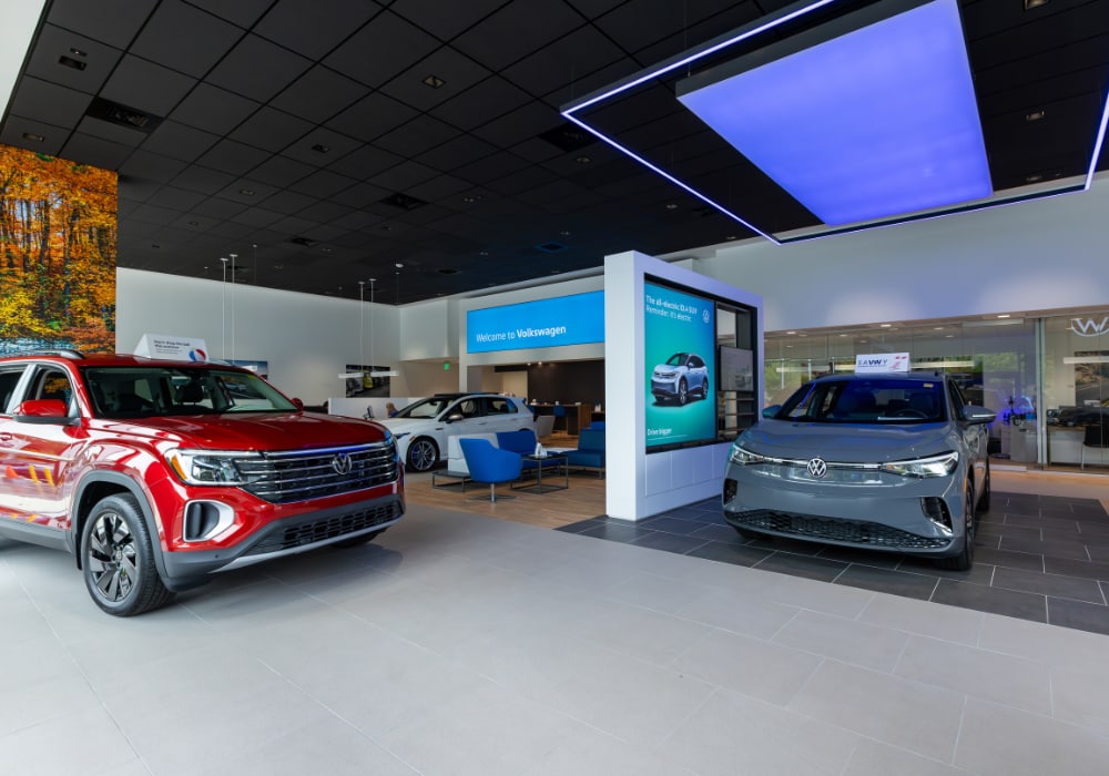 Interior of Flow Volkswagen of Asheville dealership. There are three Volkswagen cars parked inside the showroom floor