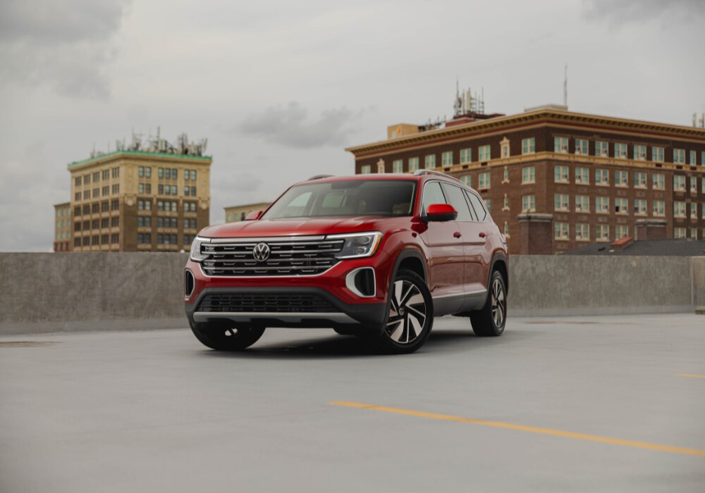 Red Volkswagen Atlas SUV parked on top of a parking garage with tall buildings in the background