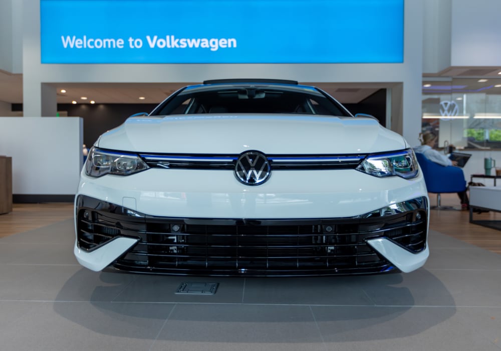 volkswagen-certified-pre-owned-cars-asheville.png White Volkswagen sedan parked inside a Volkswagen dealership with a Welcome to Volkswagen sign in the background