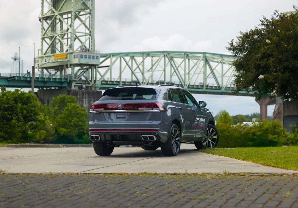 Exterior view of the rear of a new Volkswagen Atlas Cross Sport parked in front of a large bridge