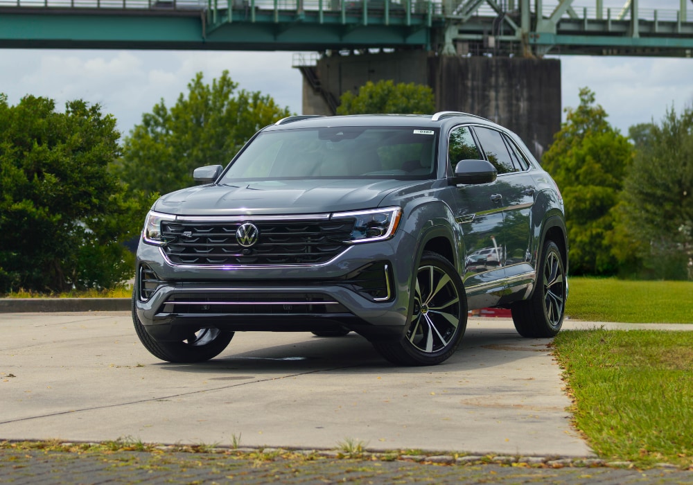 2025-volkswagen-atlas-cross-sport.png 2025 Volkswagen Atlas Cross Sport parked on a paved surface in front of a bridge