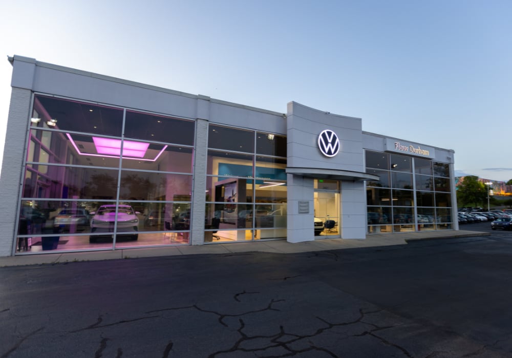 Exterior storefront of the Flow Volkswagen or Durham dealership. The VW logo is lit up on the dealership