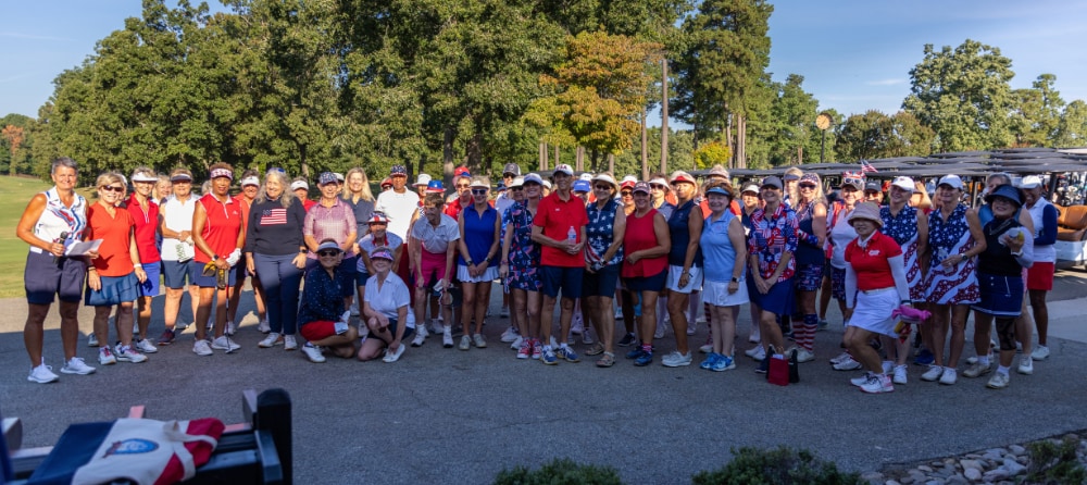A group of people wearing red, white, and blue posed in front of a golf course