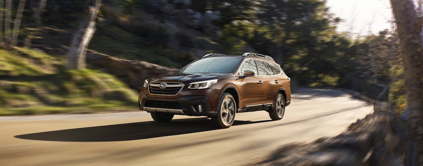 A brown 2022 Subaru Outback Touring is shown driving on a forest road.