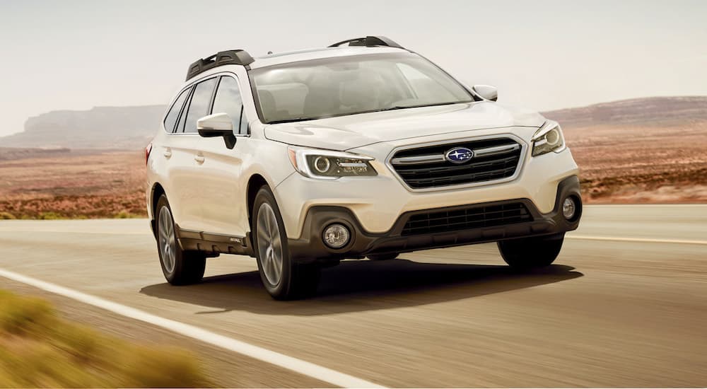 A white 2019 Subaru Outback is shown from the front driving on an open highway.