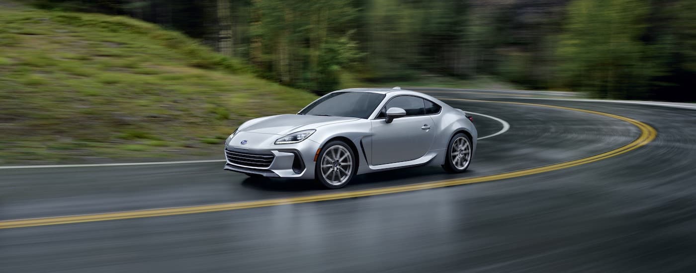 A silver 2023 Subaru BRZ is shown rounding the corner on a wet road.