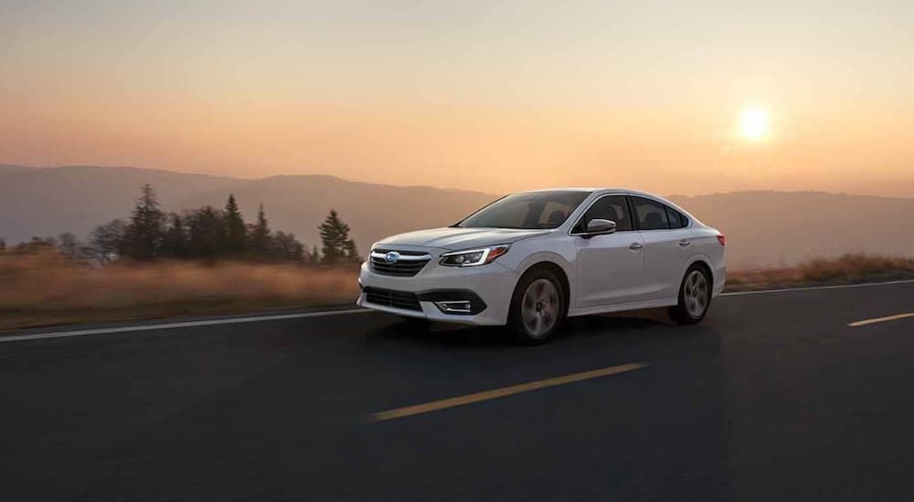 A white 2021 Subaru Legacy is driving past mountains at sunset.