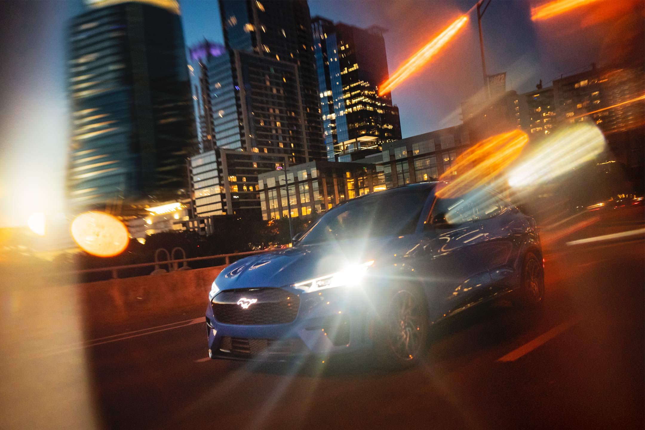 A Mustang Mach-E being driven in the city as the sun sets