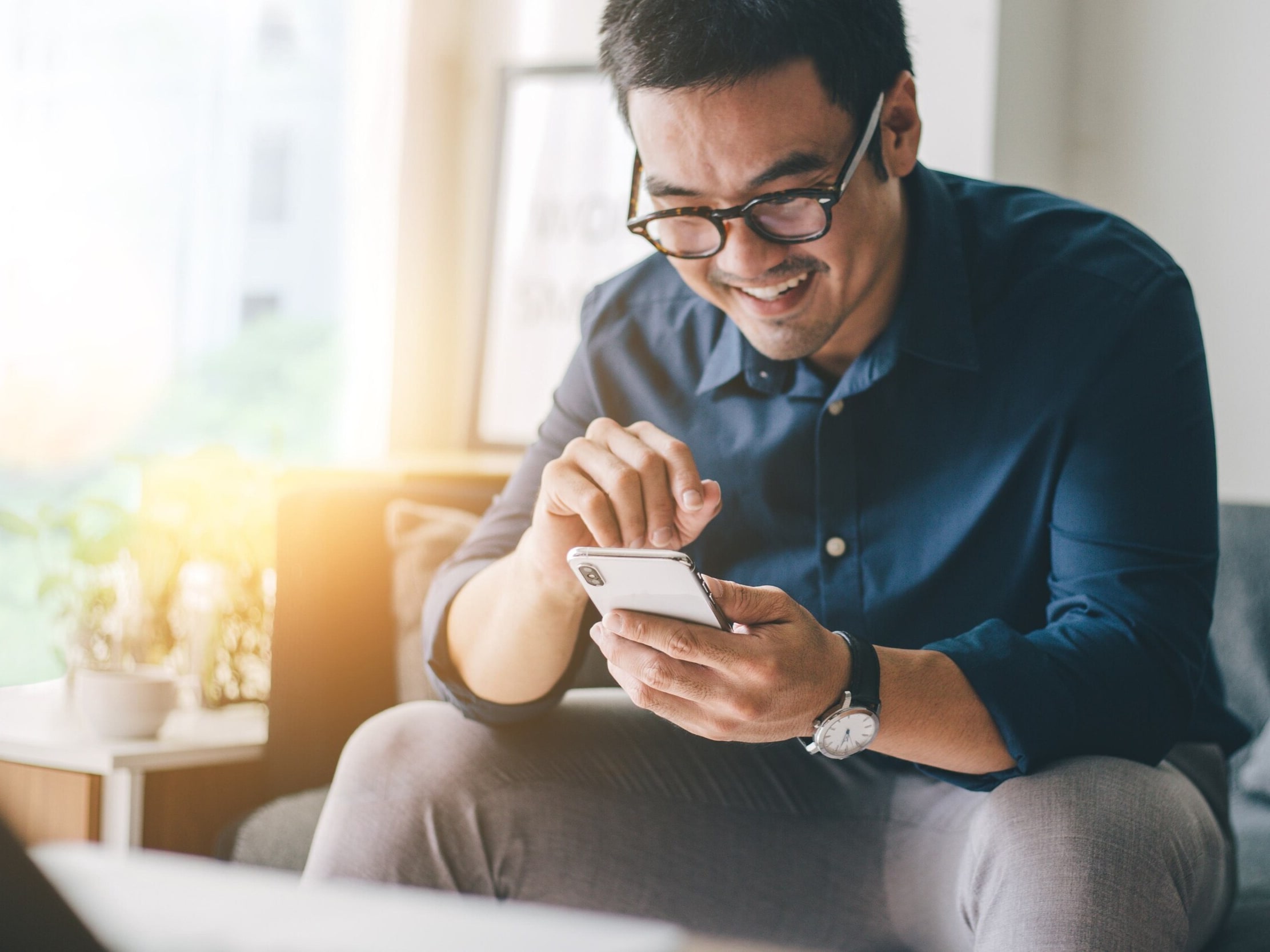  Smiling person in glasses sits in a well-lit room and uses their smartphone to learn about Flex Buy financing. 