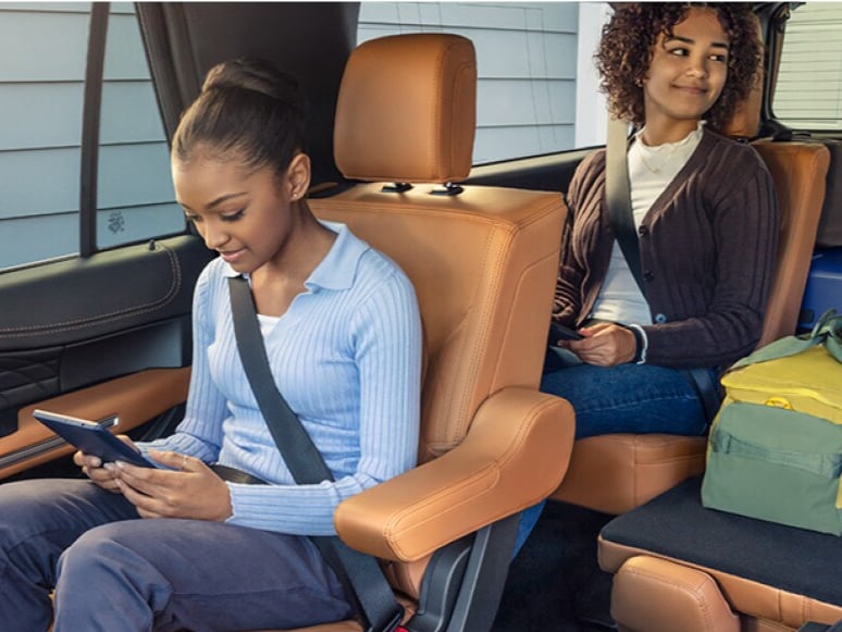  Two smiling children using mobile devices while sitting in the second and third rows of a Ford SUV.