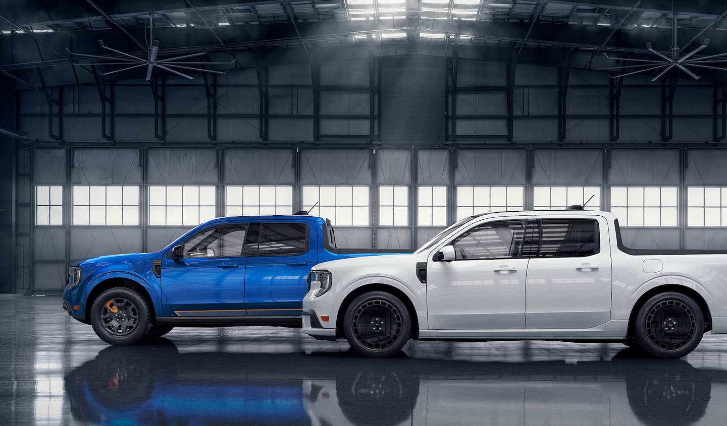 A white Ford Maverick® Lobo™ pickup in front of a blue Ford Maverick® TREMOR® pickup, parked in an aircraft hangar.