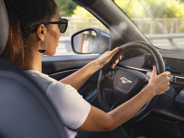  An over the shoulder view of a woman behind the wheel of a Mustang Mach-E<sup>®</sup> SUV driving over a bridge.