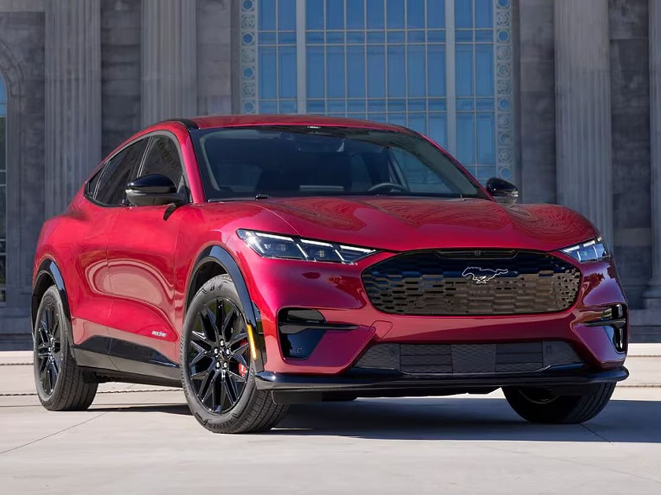  A red 2025 Ford Mustang Mach-E<sup>®</sup> SUV parked in front of an ornate concrete building with pillars and stained glass.