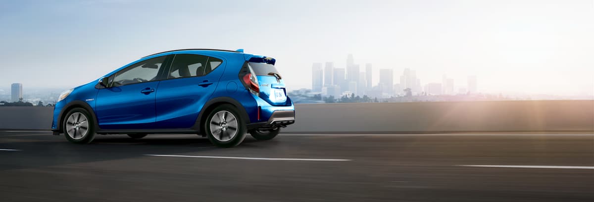 A blue 2019 Toyota Prius C driving down a highway outside of a city