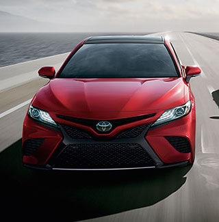 A red 2019 Toyota Camry driving down a bridge