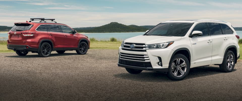 A red & white Toyota Highlander parked by a lake