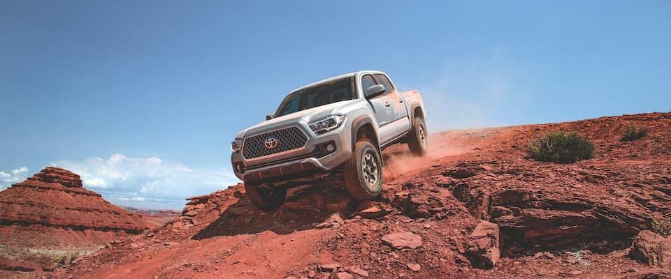 A silver 2019 Toyota Tacoma offroading over a hill
