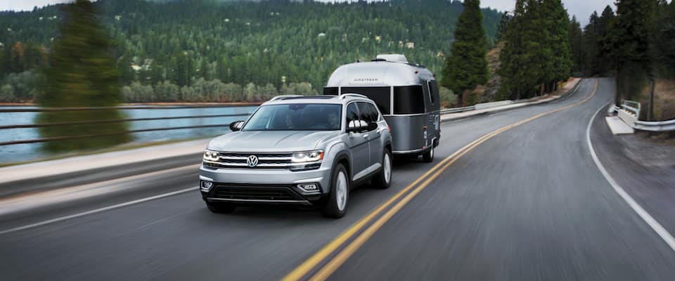 2019 Volkswagen Atlas A silver 2019 Volkswagen Atlas hauling a trailer down an open road by a lake