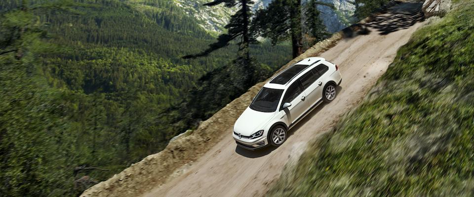 A white VW Golf Alltrack driving down a dirt hill