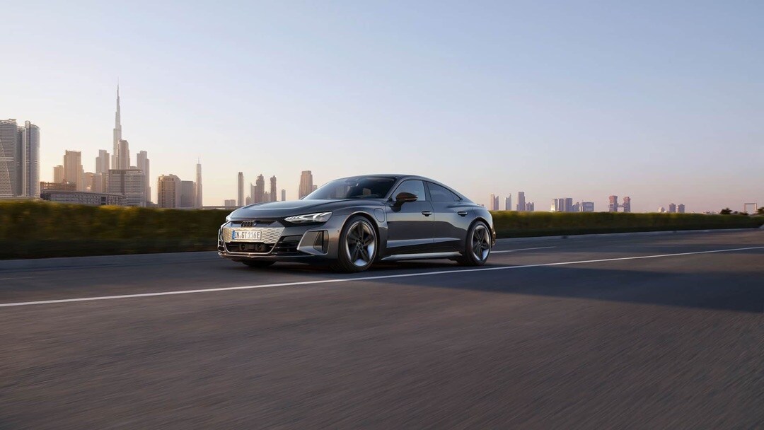 Vue 3/4 avant de la Audi RS e-tron GT 2023 roulant sur une route avec une ville en arrière-plan.