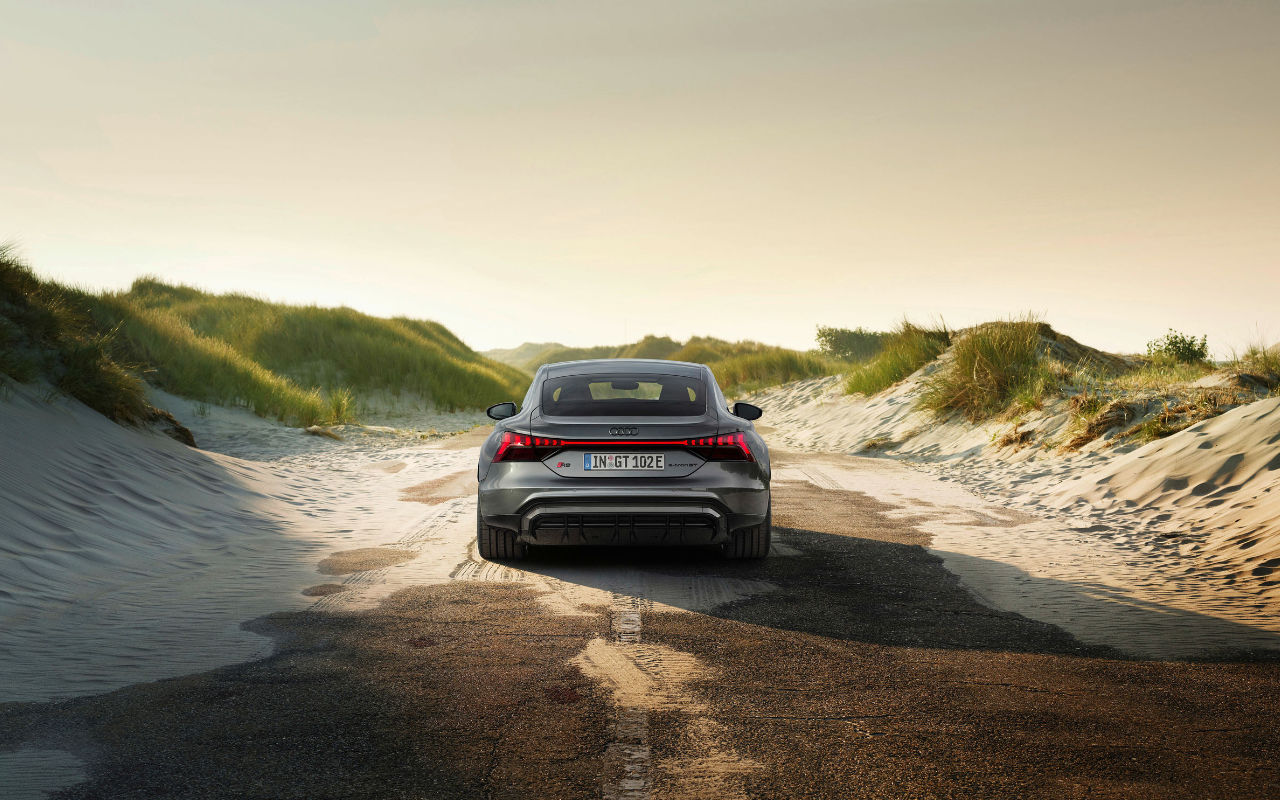 vue arrière d'une Audi E-tron GT 2023 sur une route bordée de dunes de sable et d'herbe