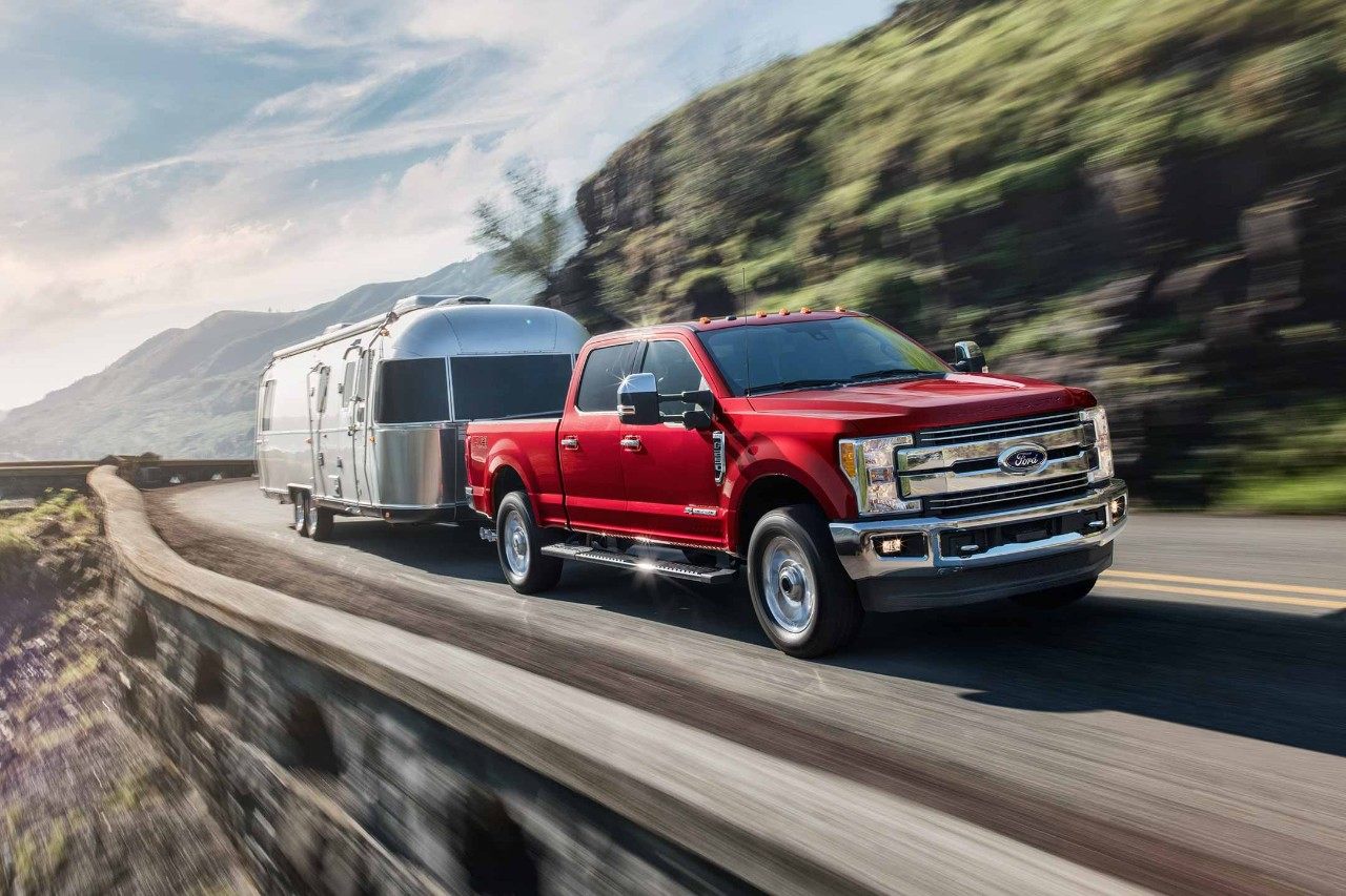 New 2018 Burgundy Ford F250 Pickup Truck Towing a Chrome Camper Over a Mountain Road