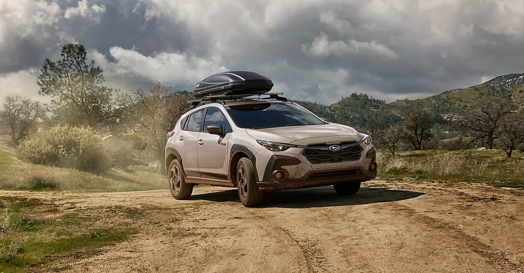 2025 Subaru Crosstrek driving off-road with a roof cargo box, showcasing rugged capability and adventure-ready design.