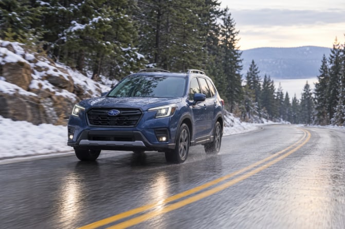 Subaru SUV driving on a wet, snowy mountain road.