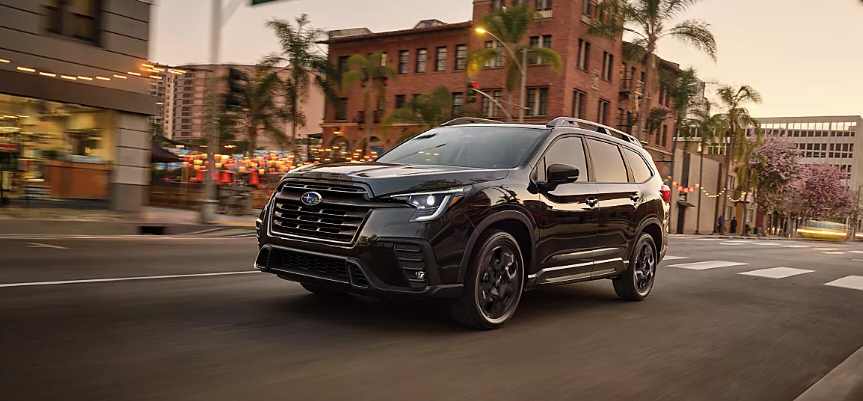 A black 2026 Subaru Ascent driving through a city street at sunset.