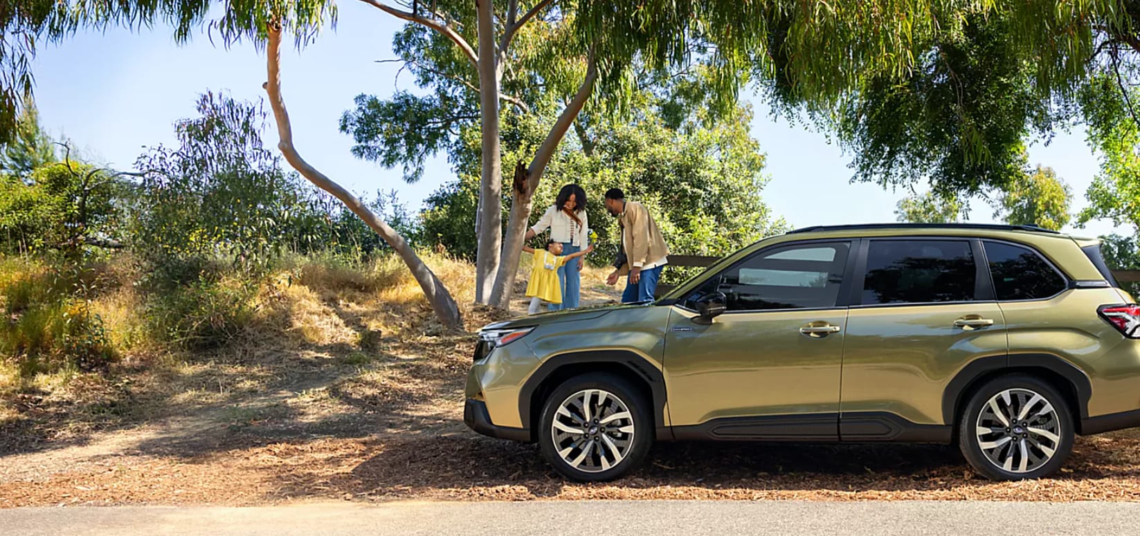 Green 2026 Subaru Forester Hybrid parked with family playing next to it.