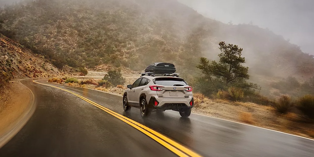 2026 Subaru Crosstrek driving on a wet mountain road in the rain, showcasing all-weather capability and stability.