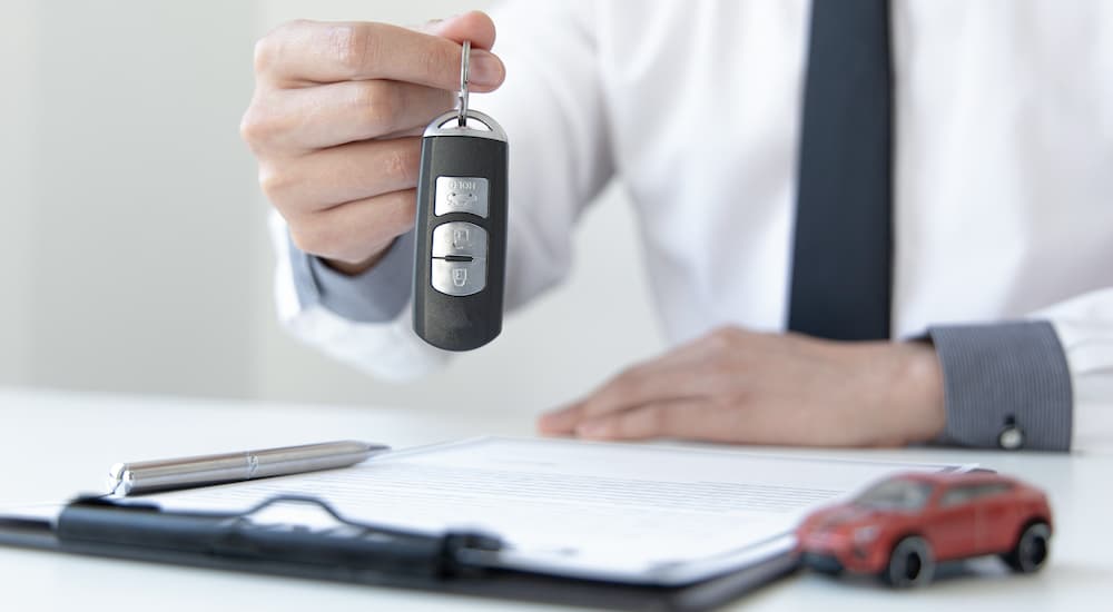 A person is shown holding a car key over a clipboard.