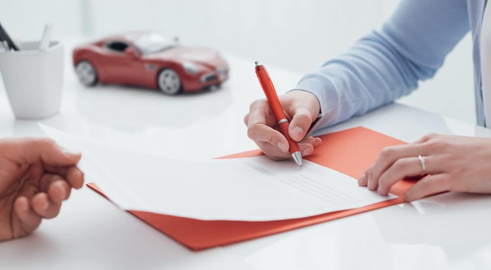 A person is shown signing Chevrolet financing paperwork next to a toy car.