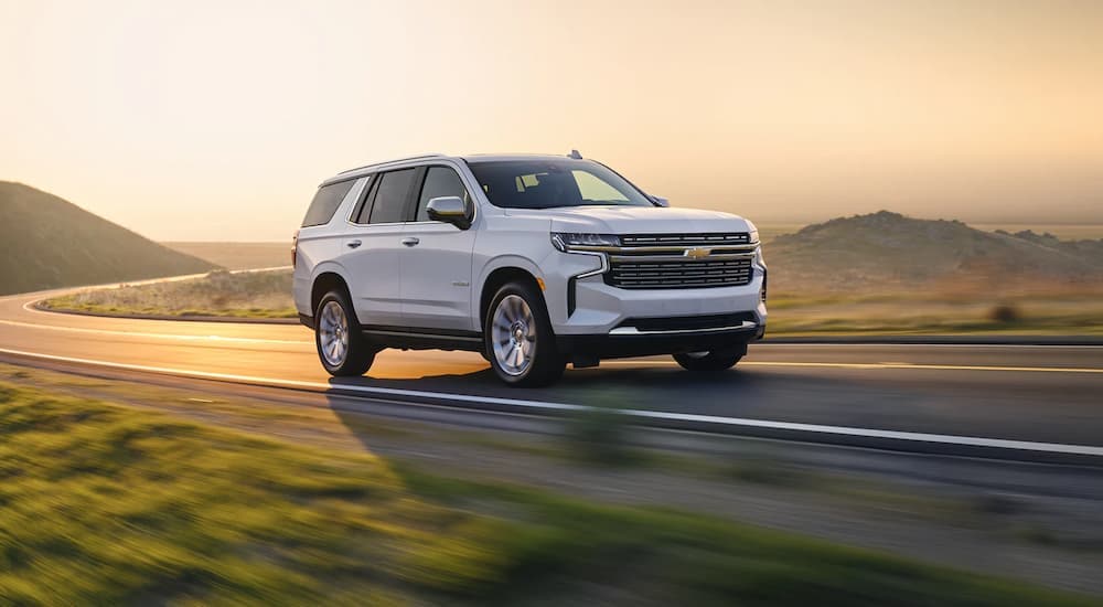 A white 2022 Chevy Tahoe Premier is shown driving on an open road near a Roseville Chevrolet dealership.