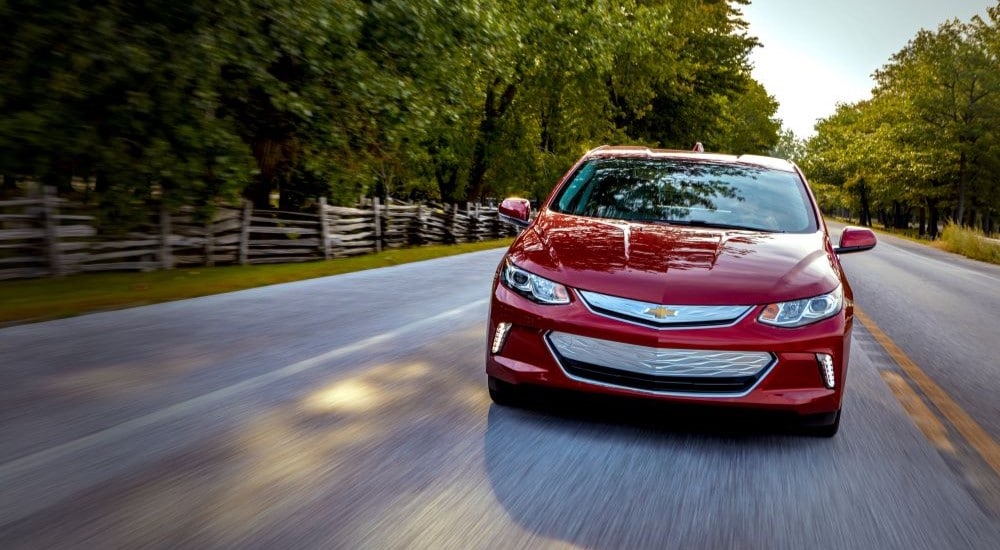 A red 2019 Chevy Volt is shown from the front driving on a tree-lined road.