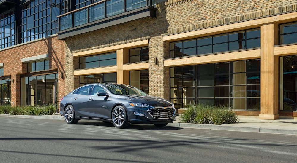 A grey 2020 Chevy Malibu is shown in front of a brick building Rancho Cordova Chevy dealer.