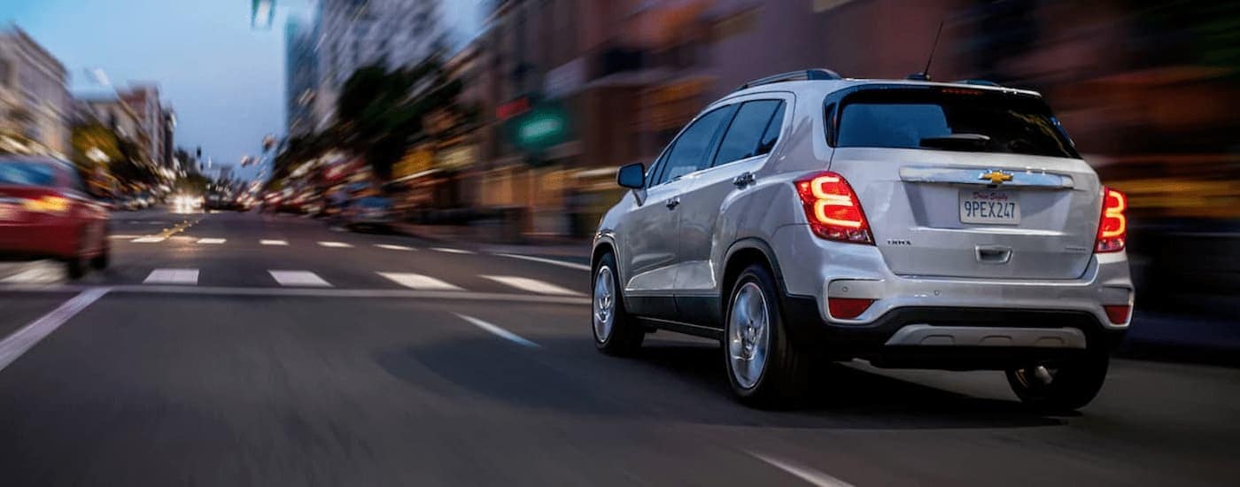 A silver 2020 Chevy Trax is shown from the rear driving on a city street.