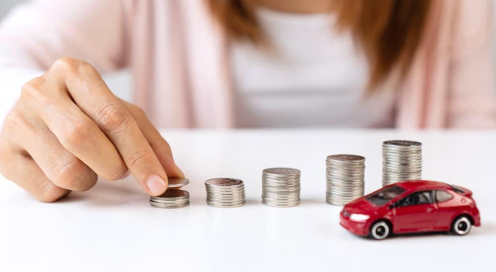 Close-up of a person stacking coins next to a toy car.