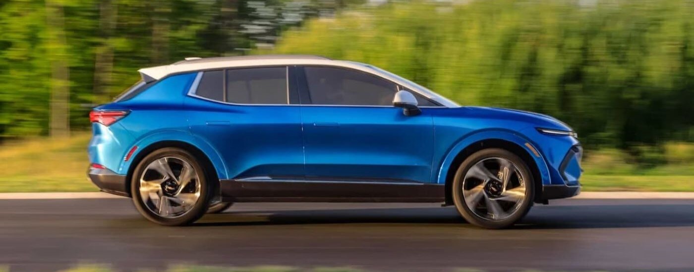 A blue 2024 Chevy Equinox EV is shown from the side driving past tall grass and trees.