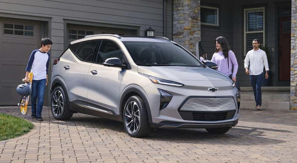 A family approaching a 2023 white Chevy Bolt EUV parked in front of their modern home