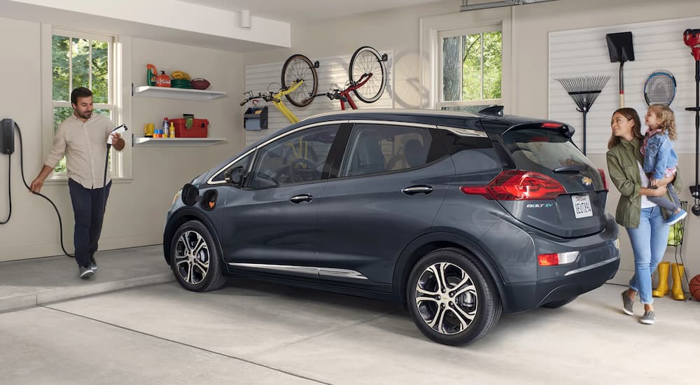 Inside his home garage, a man prepares to plug in his grey 2021 Chevy Bolt EV