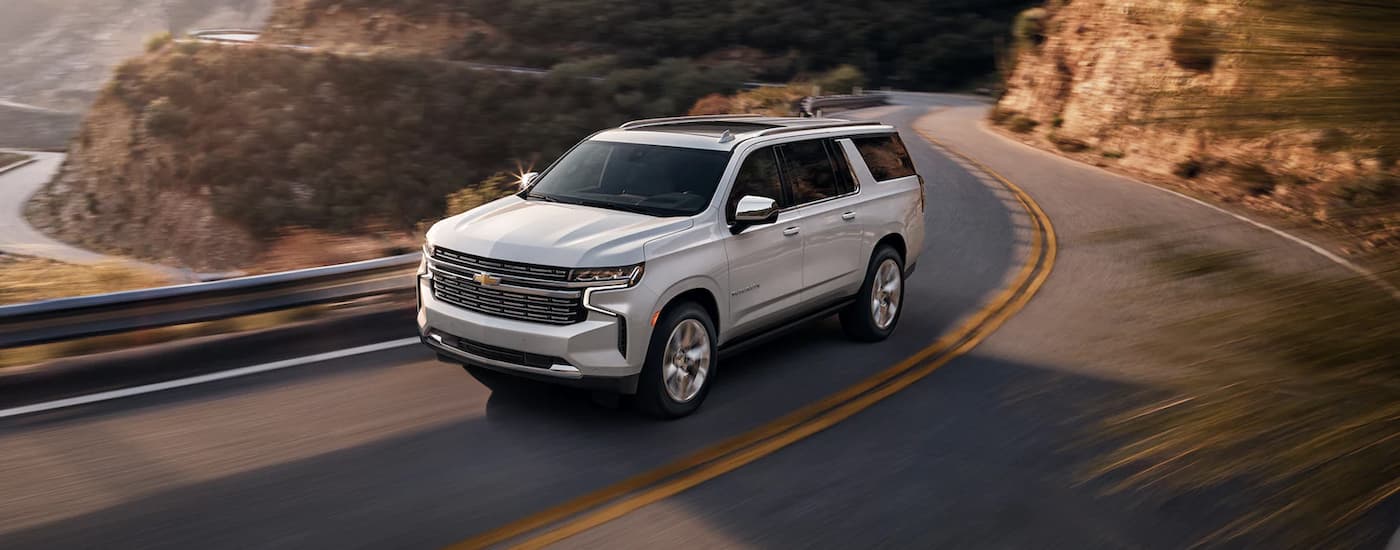 A white 2022 Chevy Suburban LT is shown driving on an open road after viewing used Chevy SUVs for sale.