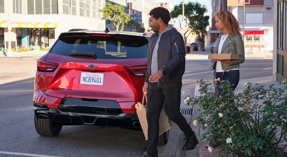 A couple walking to their red 2023 Chevy Blazer RS after visiting a restaurant.
