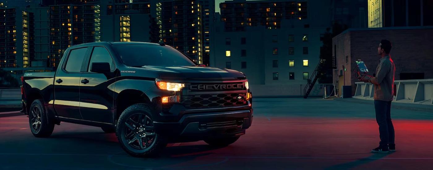 A black 2023 Chevy Silverado 1500 Custom is shown parked in a city at night.