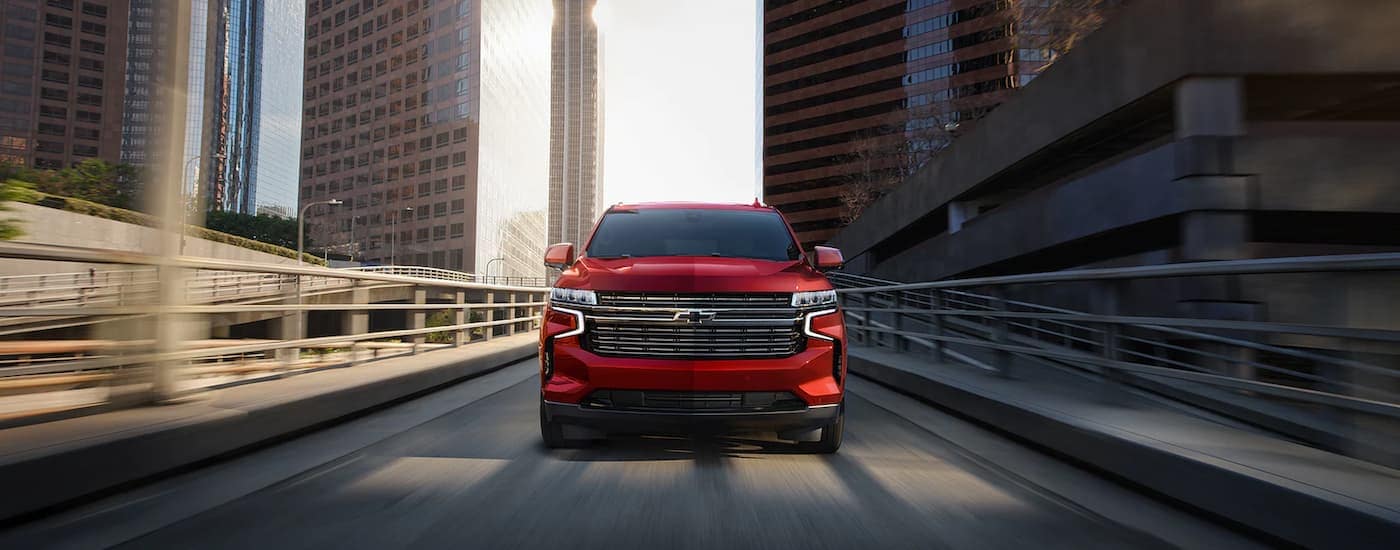 A red 2023 Chevy Tahoe is shown from the front driving on a city highway.