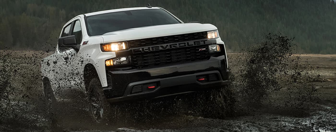 A white 2022 Chevy Silverado 1500 Trail Boss Z71  is shown off-roading in the mud.