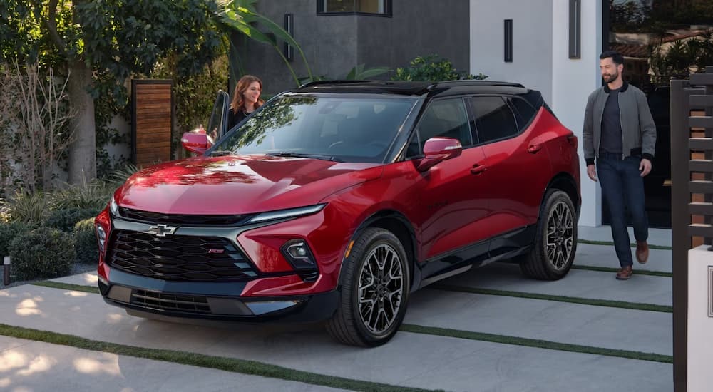 A man and woman approach a red 2023 Chevy Blazer RS parked in the driveway
