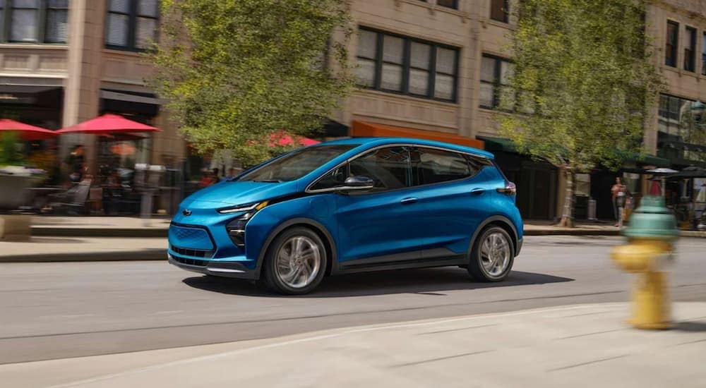 A blue 2023 Chevy Bolt EV driving on a modern city street.