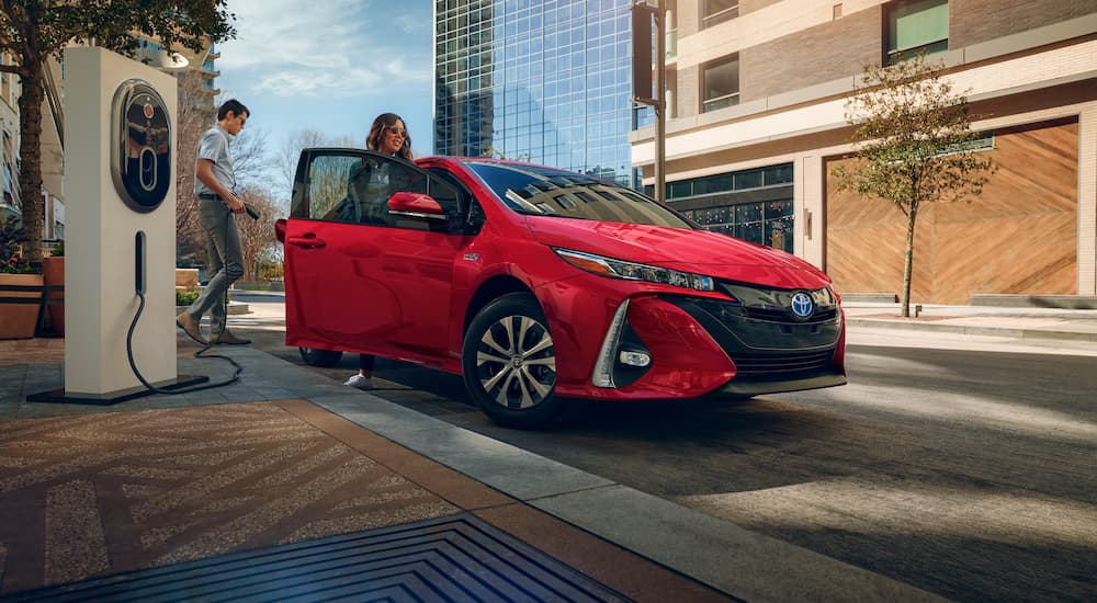 A man and woman prepare to charge their red 2021 Toyota Prius Prime Limited at a downtown charging station