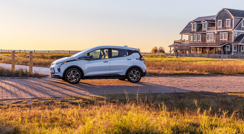A light blue 2022 Chevy Bolt EV is shown from the side near a beach house.